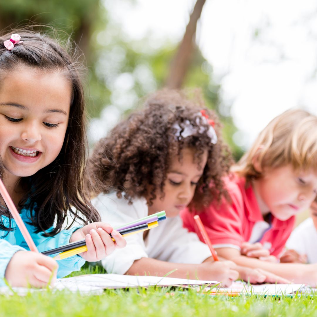 children lying down in the grass drawing with markers