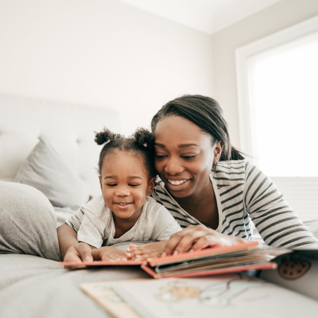 A mother and daughter laying on a bed reading a book
