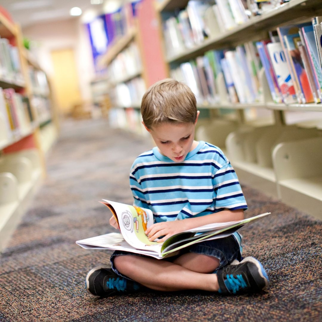 A preschool-aged child in the library looking at a book