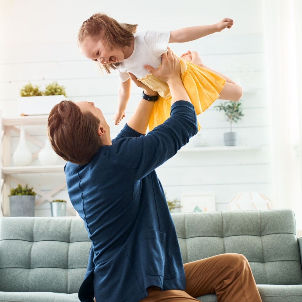 A father holding his daughter up in the air while she puts her arms out