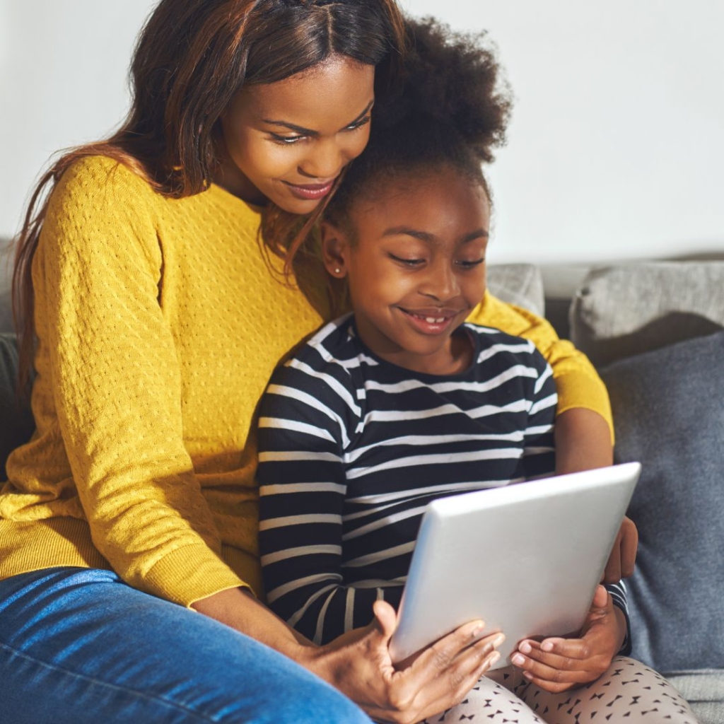A mother and daughter on a couch looking at a tablet together