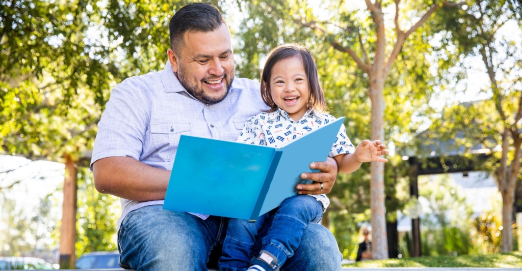 A father and son reading a book outside