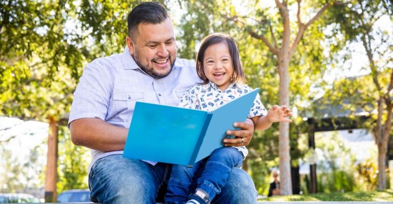 A father and son reading a book outside