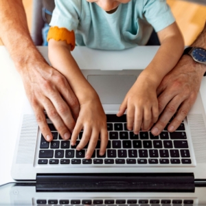 an adult and child typing on a laptop at the same time