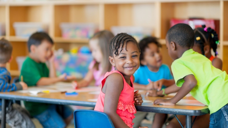 a little girl smiling at a desk